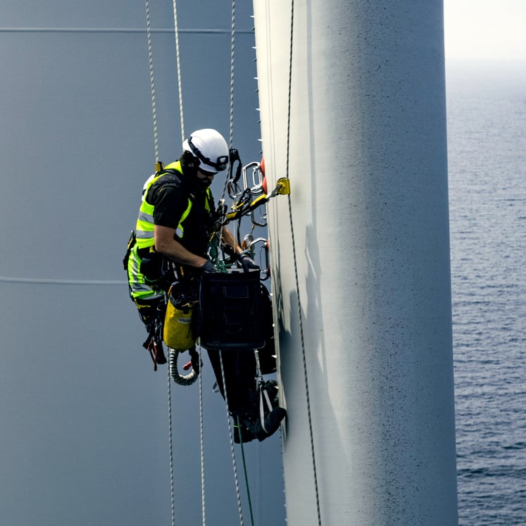 Mann in Schutzausrüstung an einem Offshore-Windrad