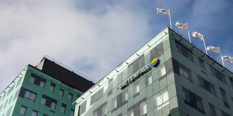 Ein modernes Bürogebäude mit einer grün getönten Glasfassade, Fahnen auf dem Dach und einem Vattenfall-Logo. Ein modernes Bürogebäude mit einer grün getönten Glasfassade, Fahnen auf dem Dach und einem Vattenfall-Logo.