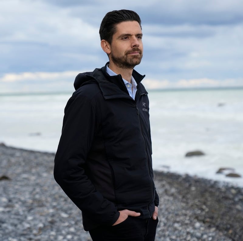 Tim Wilms - am Strand stehend und auf das Meer blickend.