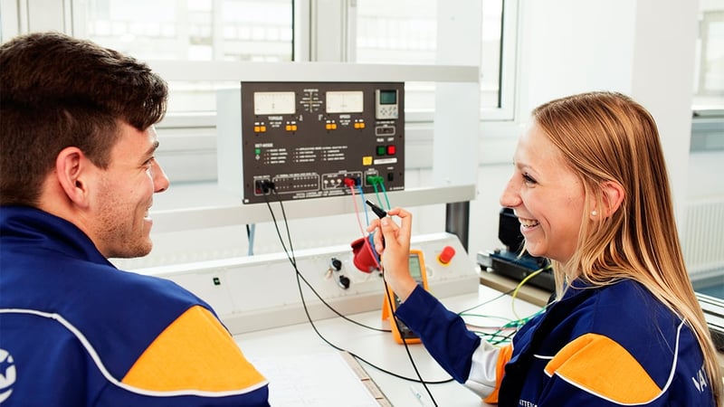 Zwei junge Vattenfall-Servicetechniker lächelnd vor einer Schalttafel sitzend