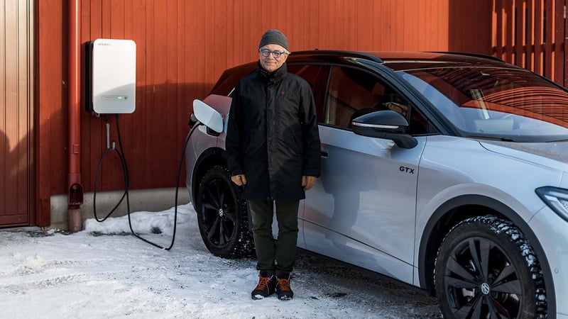 Ein Mann steht vor seinem Elektroauto. Das Auto ist mit der Ladestation verbunden.