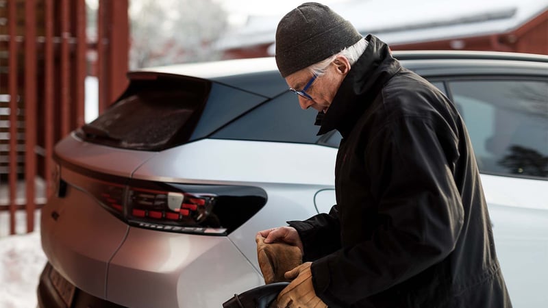 Ein Mann neben seinem Elektroauto in einer Winterlandschaft