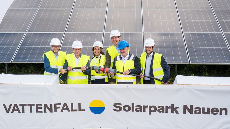 Personen der beteiligten Unternehmen und Institutionen stellen vor dem Solarfeld eine provisorische Kabelverbindung her