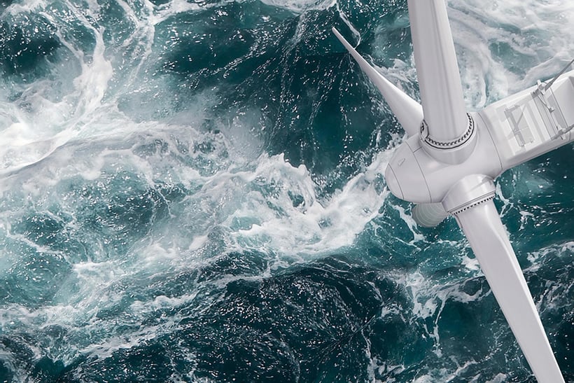 Nahaufnahme einer Windkraftanlage über schäumendem Meerwasser.