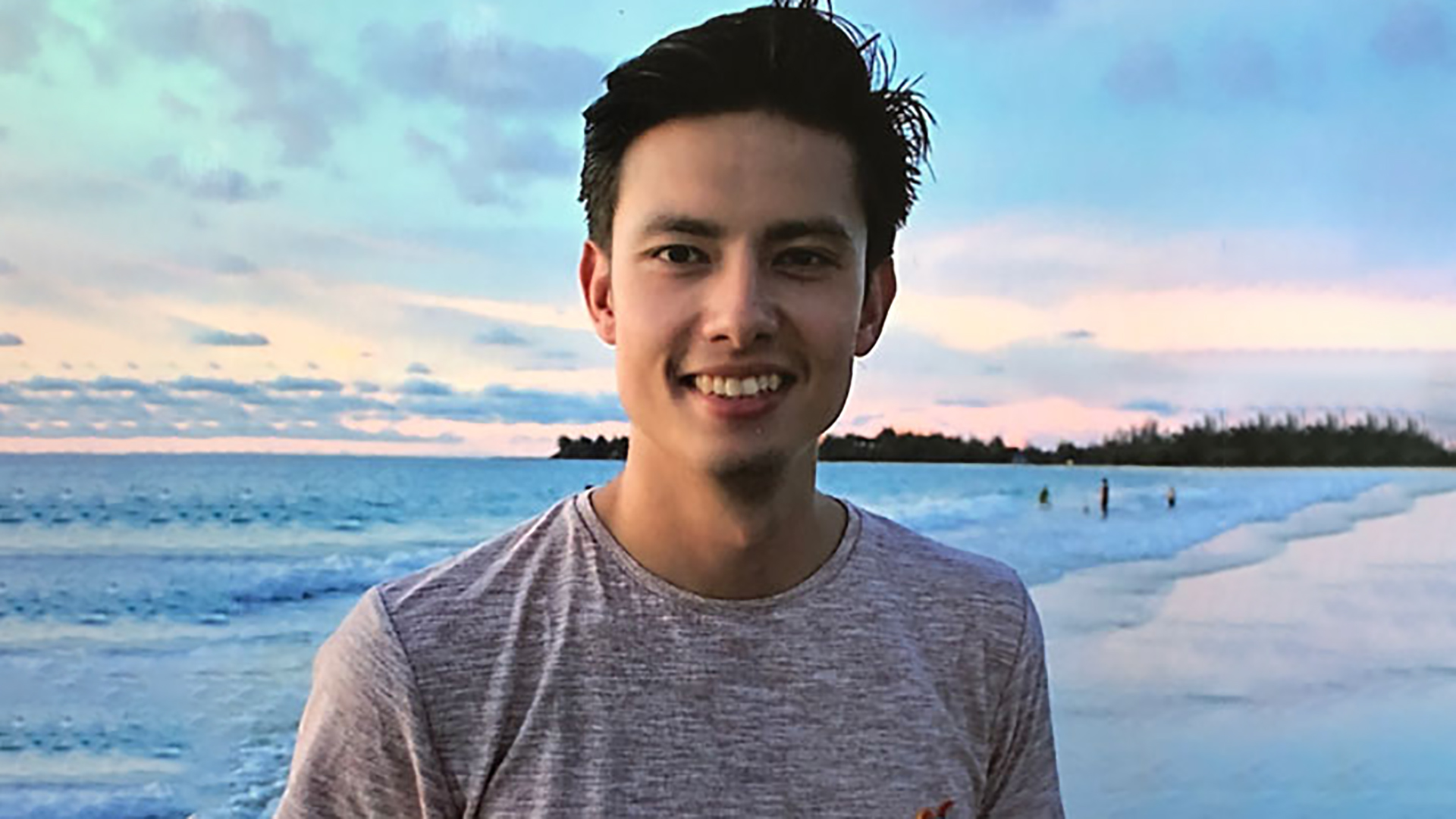 Tim Hoogvliet - ein junger Mann lächelt in die Kamera, im Hintergrund ein Strand
