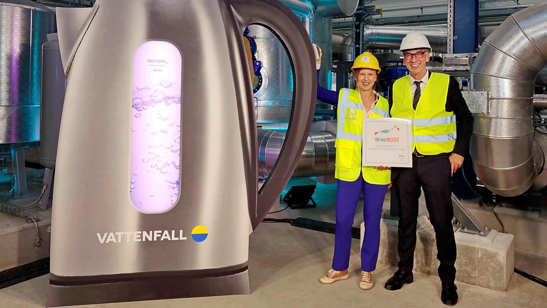 Inbetriebnahme Power-to-heat Anlage in Berlin  - zwei Personen vor einem riesigem symbolisierten Wasserkocher