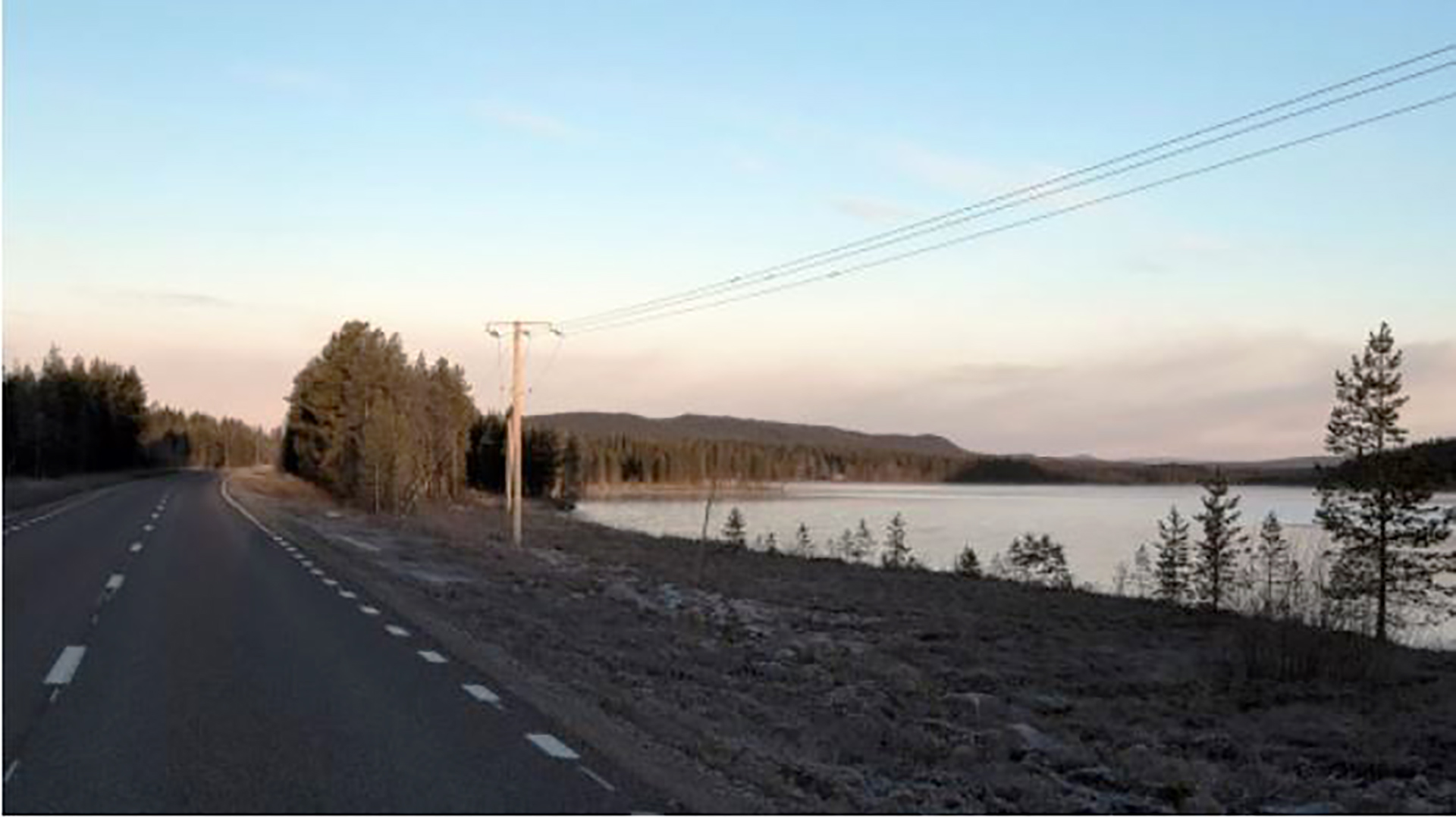 Landstraße, einfache Stromleitung, am See vorbeiführend in Schweden