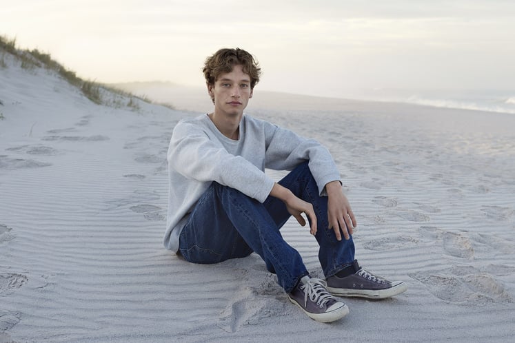 Teenagedreng, der sidder på en strand Teenagedreng, der sidder på en strand