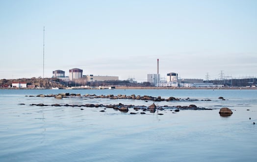 Ydinvoimalaitos meren rannalla tyynen veden ja kallioiden takana. Ydinvoimalaitos meren rannalla tyynen veden ja kallioiden takana.