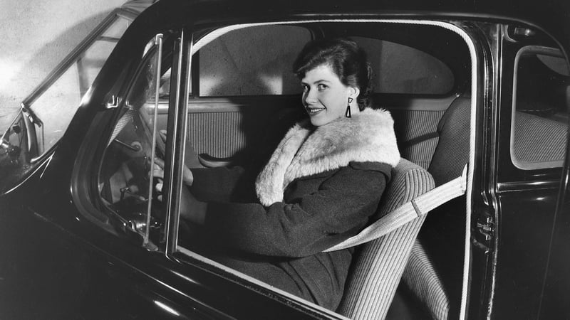 Mustavalkoinen kuva naisesta, joka istuu vanhemman mallin autossa turvavyö kiinnitettynä.