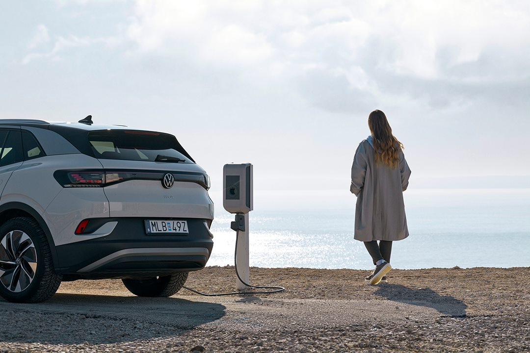 Nainen seisoo meren rannalla lataamassa sähköautoaan