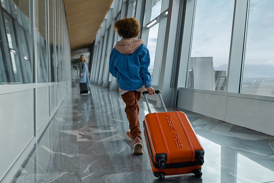 Lapsi vetää matkalaukkua, jossa teksti "Fossil free"