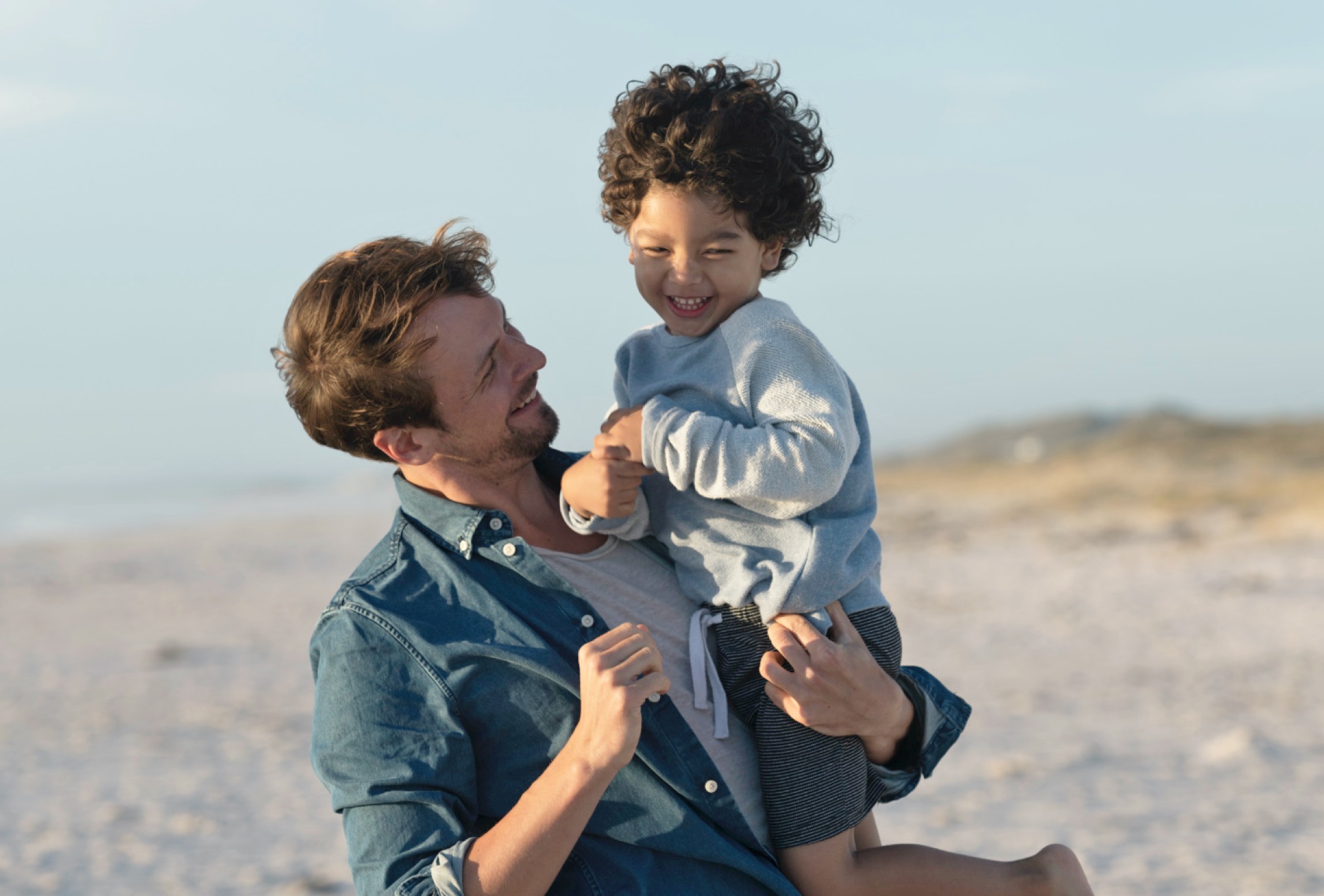 A father and a young son on the beach / Mann mit Junge auf dem Arm über den Strand gehend