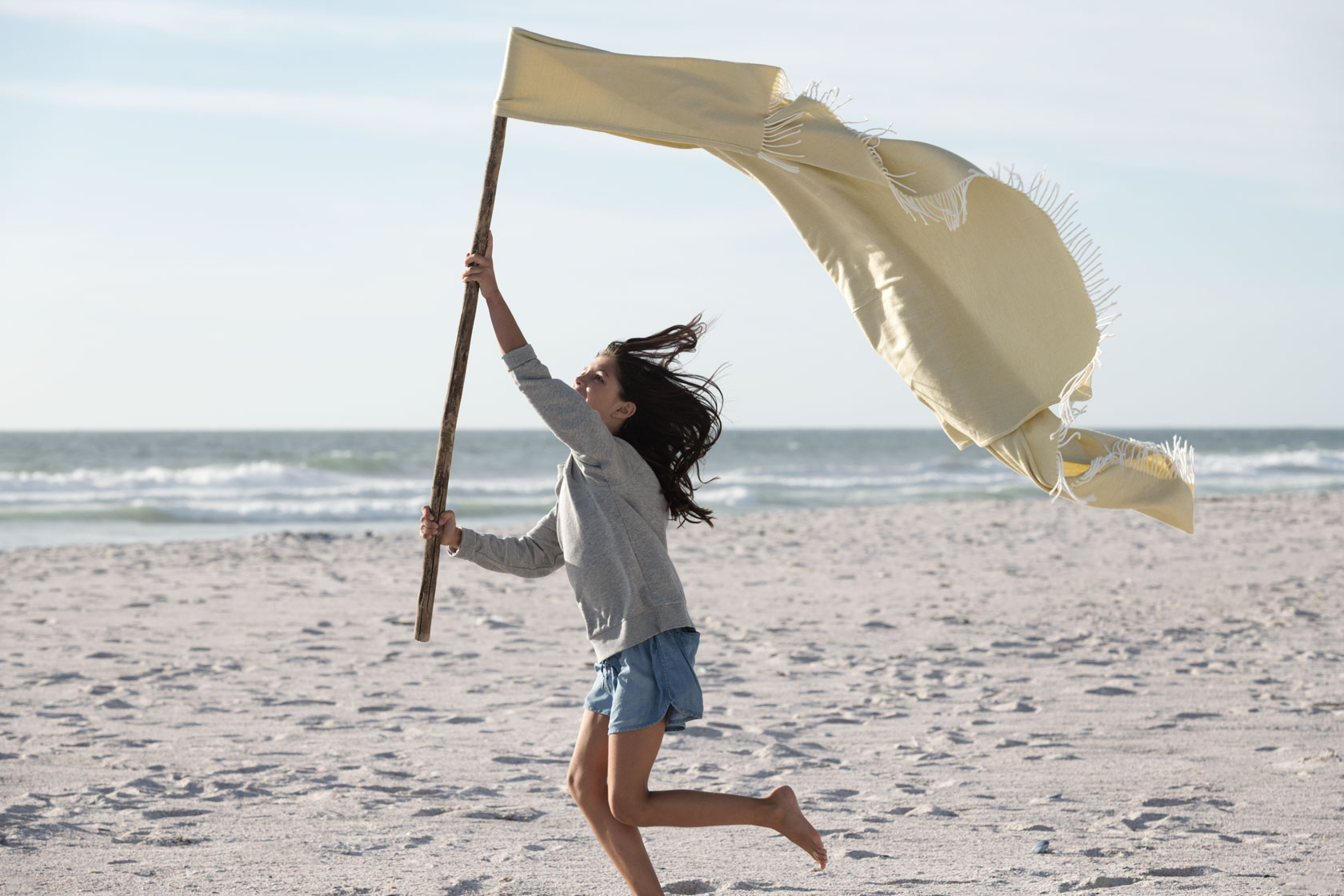 Mädchen am Strand, eine Stoffflagge schwingend