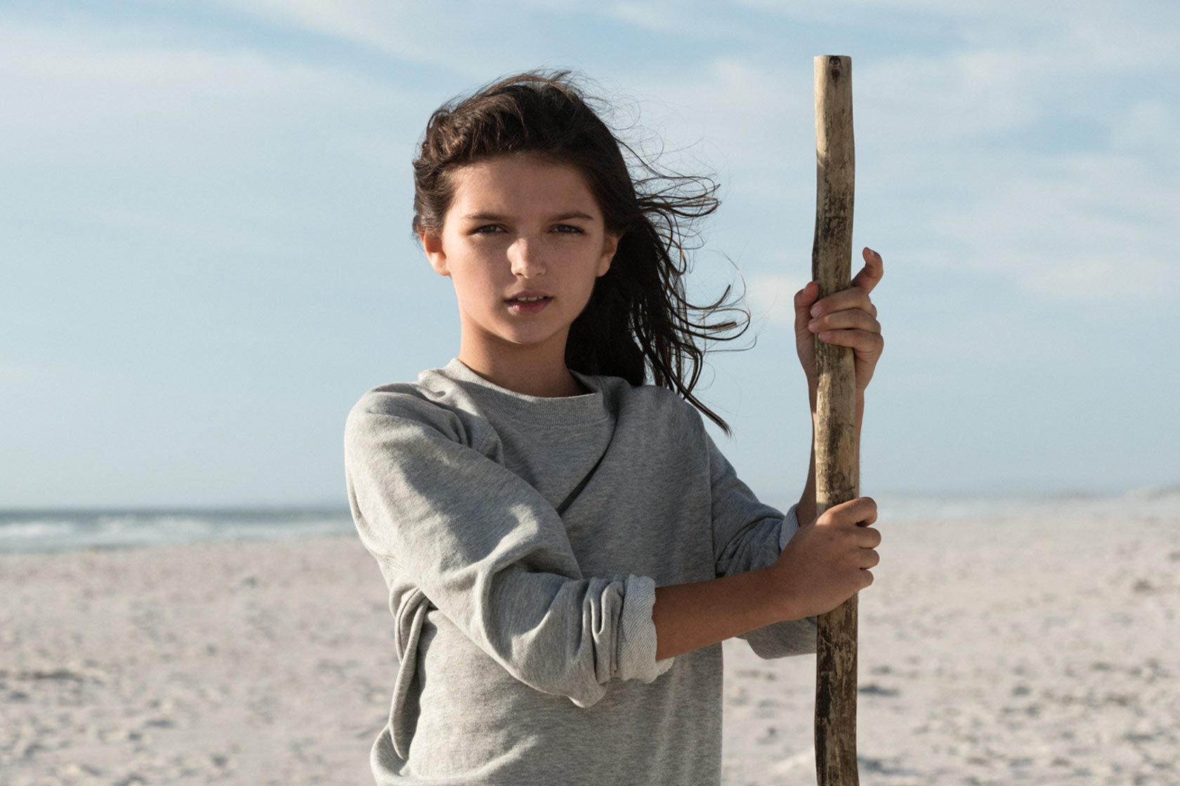 Flicka står på stranden med en pinne i handen