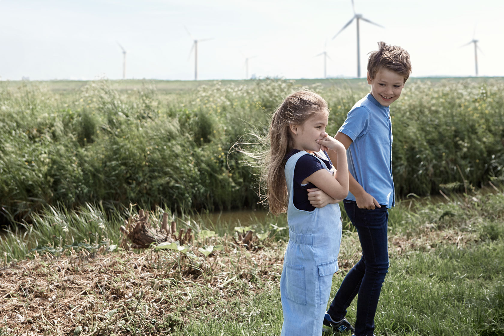 Two children standing near a field near a wind farm