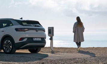 Nainen seisoo meren rannalla lataamassa sähköautoaan