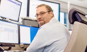 Staff sitting in front of monitors looking into camera