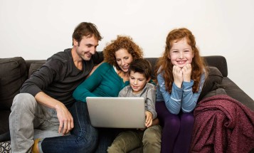 A family sitting in a sofa with a laptop
