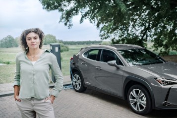 Frau im Vordergrund, Fahrzeug im Hintergrund an E-Ladesäule angeschlossen.