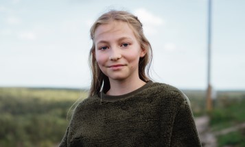 Mädchen mit grünem Pullover in die Kamera blickend