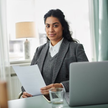 En kvinna som sitter vid en dator med ett dokument i handen