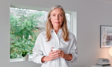 Kvinna som står i ett vardagsrum med en kopp i händerna