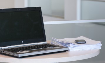 A laptop, a pile of papers and a mobile phone on a table