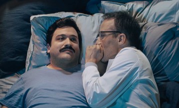 A man lies in bed trying to sleep while an engineer whispers in his ear