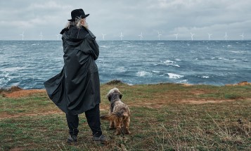 Mann steht mit seinem Hund im Wind und betrachtet das Meer