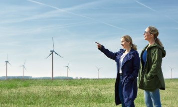 Two women standing close to a wind farm. 