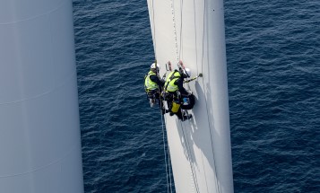 Technician in safety clothing climbing on a wind turbine rotor blade