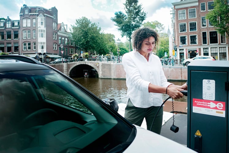 Een vrouw laadt een elektrische auto op aan een Amsterdamse gracht