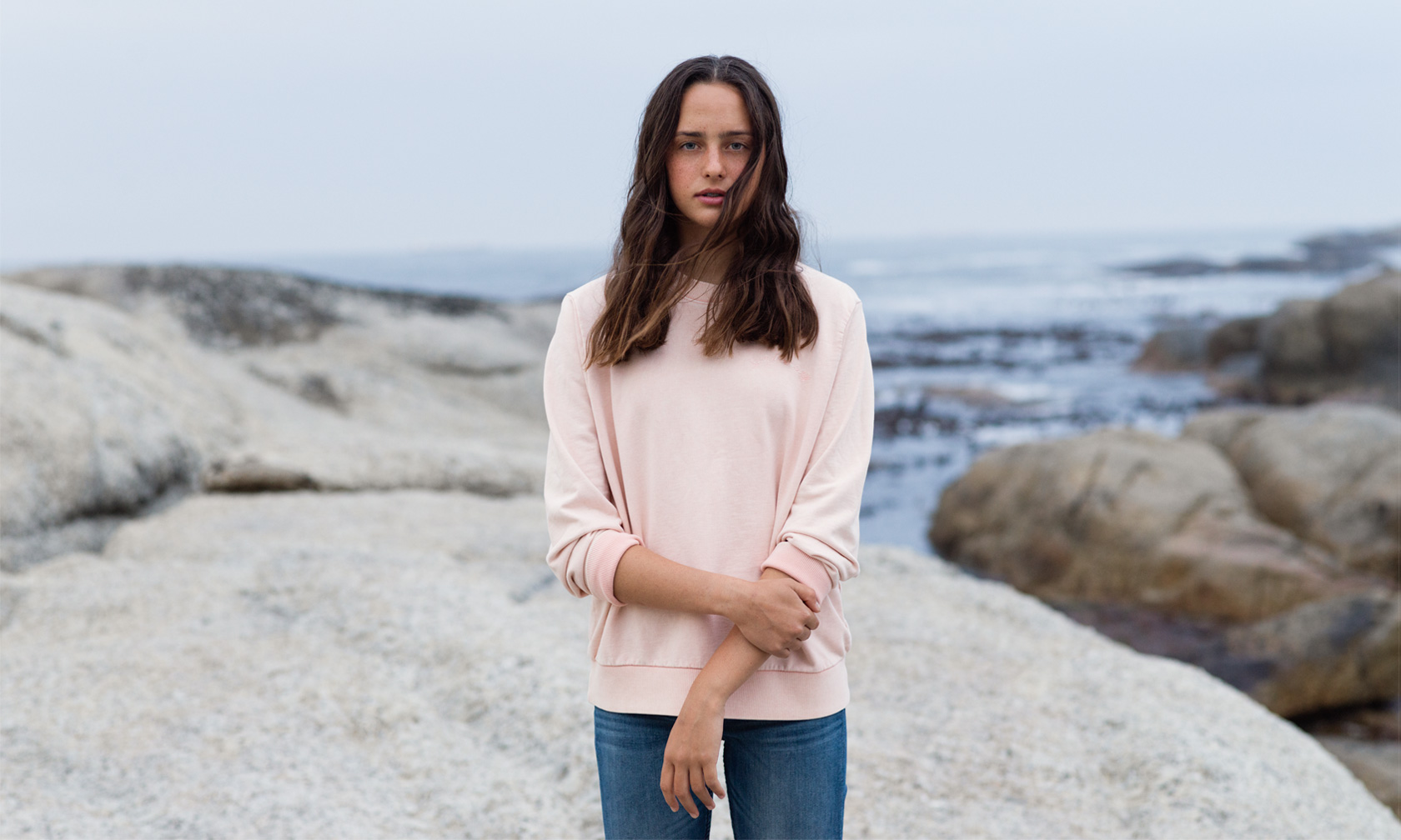 En flicka i rosa tröja på klippor vid havet
