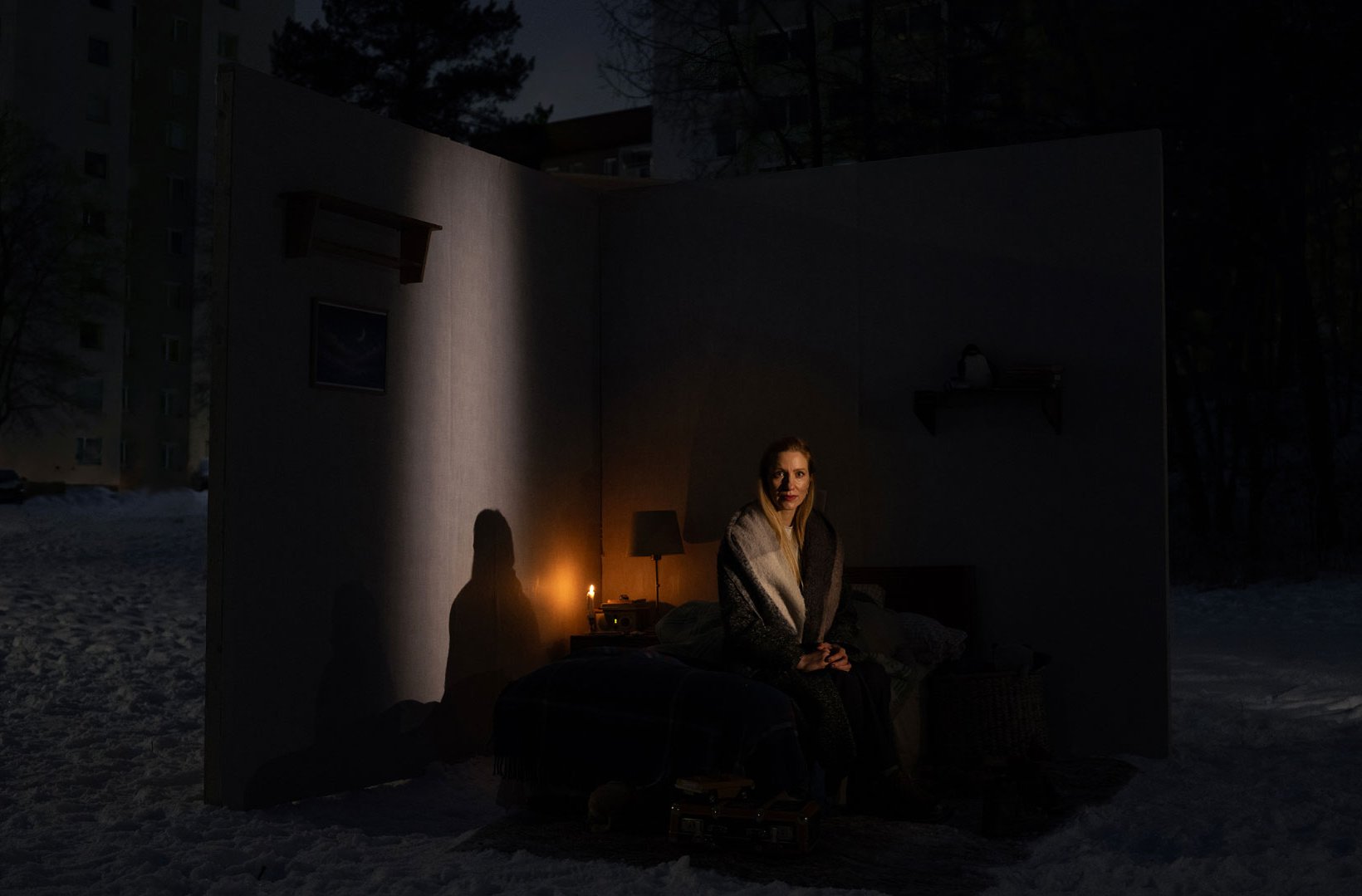 En kvinna sitter på en säng i ett svagt upplyst rum som är placerat utomhus i ett snöigt nattlandskap. En kvinna sitter på en säng i ett svagt upplyst rum som är placerat utomhus i ett snöigt nattlandskap.