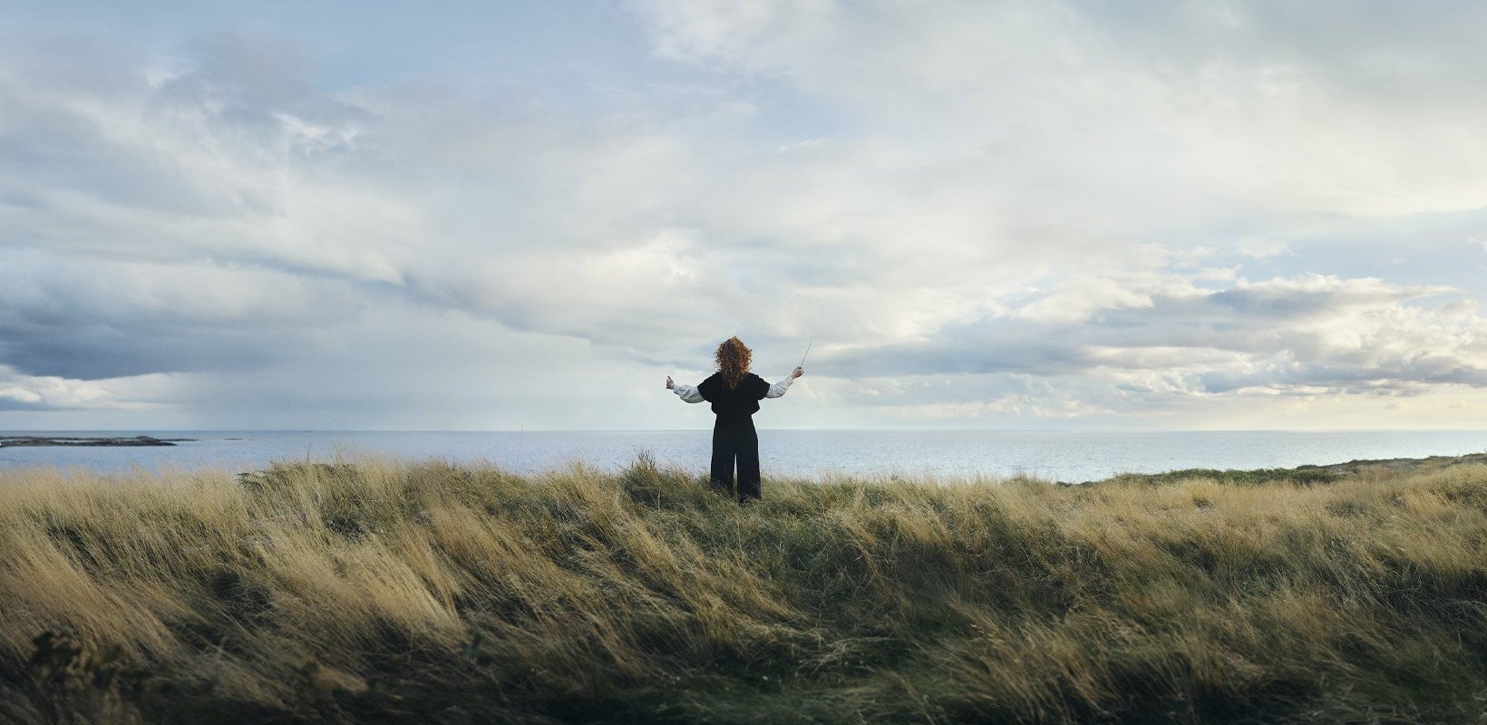 Ung person med dirigentpinne på höjd ovanför hav. Ung person med dirigentpinne på höjd ovanför hav.