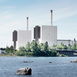 Två stora vita industribyggnader med höga skorstenar, med ett vattendrag i förgrunden.