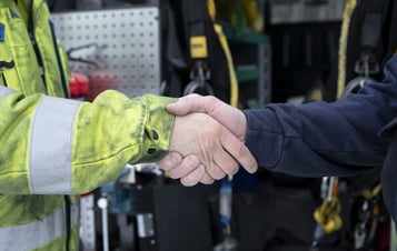 Handslag mellan två personer i arbetskläder.
