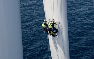 Tekniker i säkerhetskläder klättrar på ett rotorblad till en vindturbin