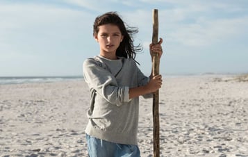 Flicka står på stranden med en pinne i handen