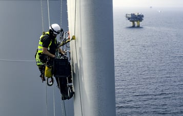 Man i skyddsutrustning klättrar på rotorblad i ett havsbaserat vindkraftverk