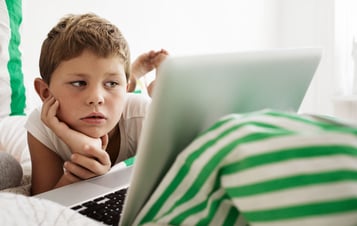 Pojke som ligger i en säng och tittar på en bärbar dator