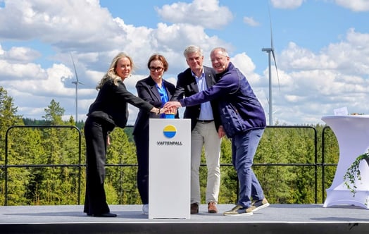 Företrädare för Vattenfall, Eksjö kommun och Volvo trycker på en knapp på ett podium med Vattenfall‑logotyp, utomhusscen med vindkraftverk och skog i bakgrunden.