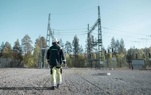 Vattenfall-medarbetare går mot kraftledningar och utrustning på grusplan omgiven av träd. Vattenfall-medarbetare går mot kraftledningar och utrustning på grusplan omgiven av träd.