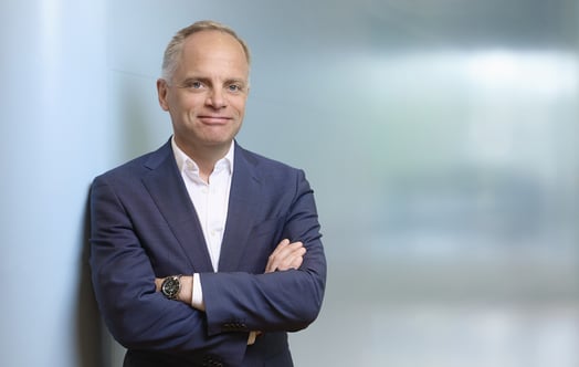 Jonas Stenbeck, privatkundschef på Vattenfall Försäljning, i blå kostym med korsade armar framför en suddig kontorsbakgrund.
