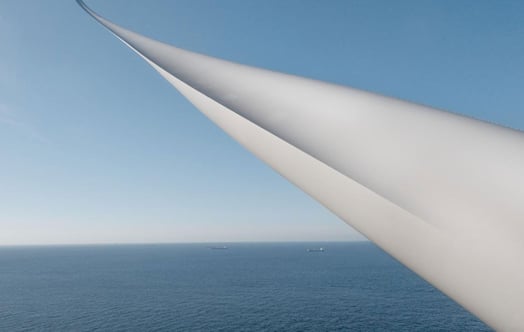 Vindkraftsblad över havet under klar blå himmel, med två fartyg vid horisonten.