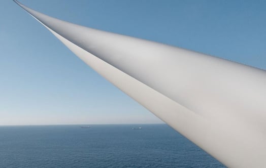 Vindkraftsblad över havet under klar blå himmel, med två fartyg vid horisonten. Vindkraftsblad över havet under klar blå himmel, med två fartyg vid horisonten.