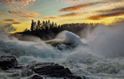 Forsande vatten över klippor i Indalsälven vid Stadsforsens vattenkraftverk i orange solnedgång. Foto: Nicklas Lindström. Forsande vatten över klippor i Indalsälven vid Stadsforsens vattenkraftverk i orange solnedgång. Foto: Nicklas Lindström.