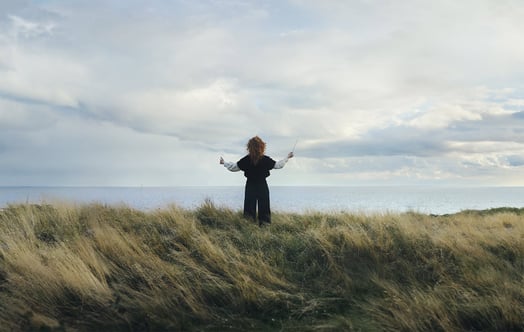 Ung person med dirigentpinne på höjd ovanför hav.