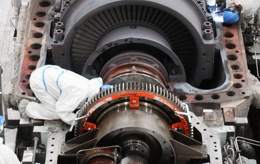 Människor i vita skydddräkter arbetar med underhåll av en generator i ett kärnkraftverk.